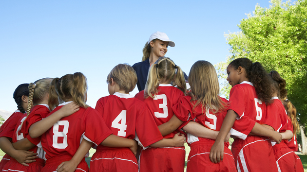 Group of children soccer players embracing standing in front of coach, back view